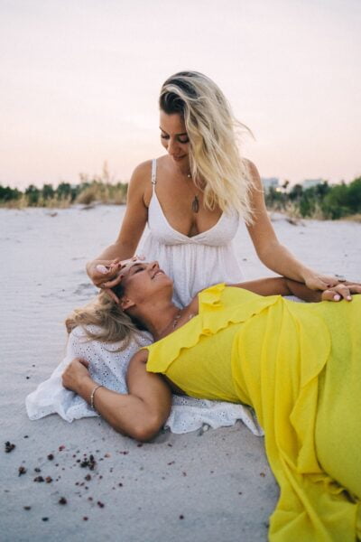 A Woman Using a Rose Quartz Roller on her Friend's Face at a Beach